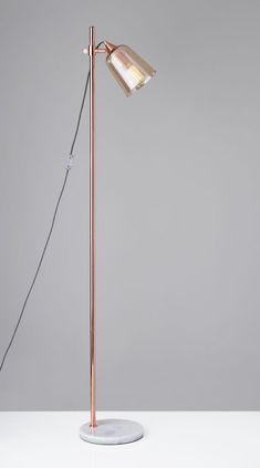 a floor lamp on a white table with a gray wall in the background and a pink shade