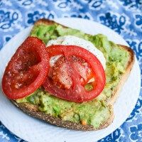 an avocado toast with tomato slices and sour cream on top, sitting on a blue patterned plate