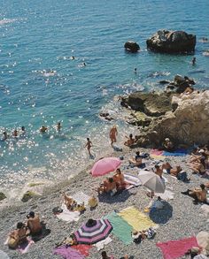 many people are on the beach with umbrellas and towels in front of the water