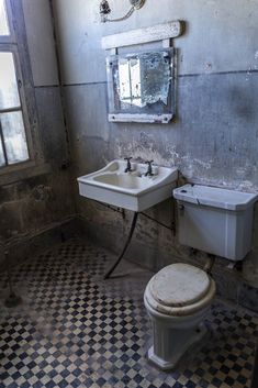 a bathroom with a toilet, sink and mirror in it's corner next to a window