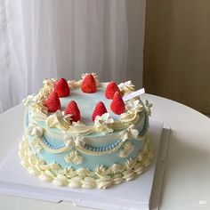 a blue and white cake with strawberries on top sitting on a table next to a window