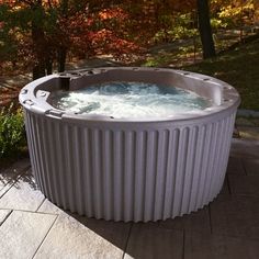 a large hot tub sitting on top of a stone patio next to trees and bushes