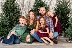 a family poses in front of christmas trees