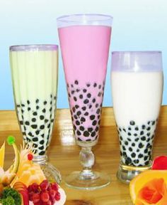 three glasses filled with different types of drinks on a wooden table next to sliced fruit