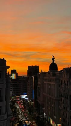 an orange and pink sky over a city at night with cars driving down the street