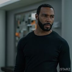 a man with a beard and black shirt standing in front of a building looking at the camera