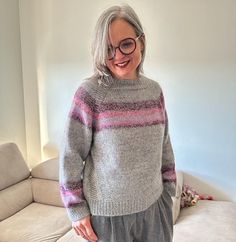 an older woman standing in front of a white couch wearing grey and pink striped sweater