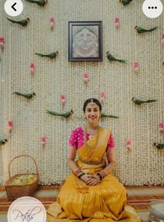 a woman sitting on the floor in front of a wall with flowers and birds hanging from it