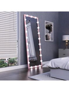 a large mirror with lights on it in a bedroom next to a bed and window