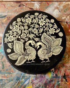 a black and gold tin with two peacocks on it's lid sitting on a wooden surface