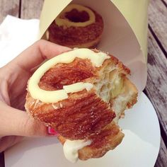 a person holding a doughnut in their hand with cream cheese on it and another donut in the background