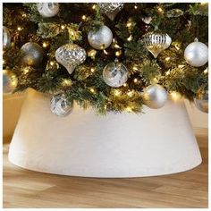 a christmas tree in a white pot with ornaments on it's top and lights around the base