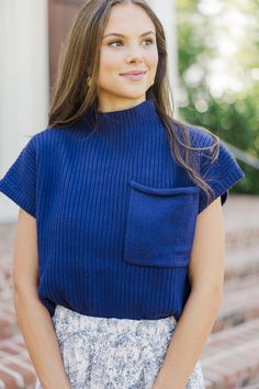 a woman wearing a blue sweater and floral print skirt with her hands in her pockets