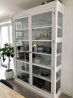 a white china cabinet with glass doors and shelves filled with plates, bowls and glasses