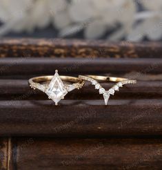 two gold rings with diamonds on them sitting on top of a piece of wooden plank