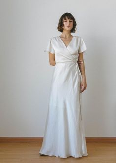 a woman wearing a white dress standing in front of a wall with her hands on her hips