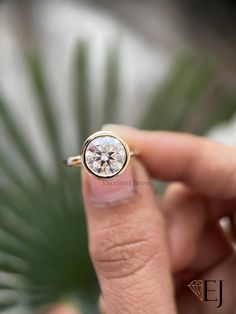 a person holding a ring with a diamond in it's middle and palm leaf behind them