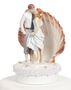 a wedding cake topper with a bride and groom kissing in front of a seashell