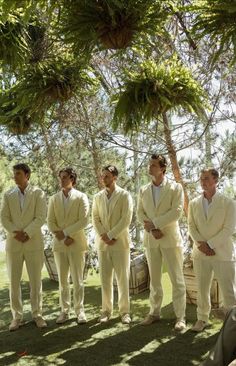 a group of men in white suits standing next to each other under a large tree