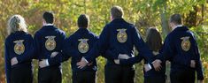 a group of people standing next to each other in front of some trees and bushes