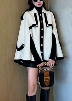 a woman in black and white outfit holding a handbag standing next to a wall