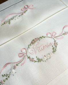 two white linens with pink ribbon and embroidered name on them, one has a wreath in the middle