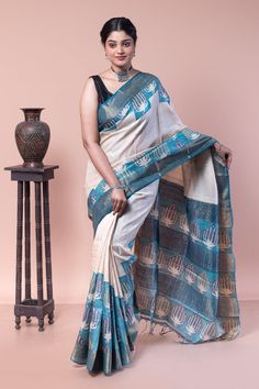 The floral buta is printed asymmetrically on this zari border saree, creating an illusion of steps. This saree is a classic example of a traditional block print represented in a modern way. COLOUR : Blue and white CRAFT : Hand block printing DIMENSIONS : Saree length 6.5 Mts., Saree width 1.14 Mts. Blouse piece inclusive. PATTERN : Floral buta Printing PRODUCT MATERIAL : Handwoven Pure Zari Border Tussar saree PRODUCT TYPE : Saree with Blouse piece WEIGHT : 450 g WASH INSTRUCTIONS : Dry Clean recommended for this product. Iron inside out. Do not bleach and expose this product to excessive heat and sunlight for long. Unstitched Tussar Silk Saree With Block Print, Cotton Silk Saree With Block Print For Festivals, Festive Tussar Silk Pre-draped Saree With Printed Border, Festival Tussar Silk Saree With Block Print, Traditional Chanderi Pre-draped Saree With Printed Border, Chanderi Pre-draped Saree With Printed Border, Festival Saree With Block Print, Chanderi Saree With Printed Border, Bollywood Block Print Cotton Silk Saree