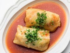 two dumplings covered in sauce and garnished with parsley on a white plate