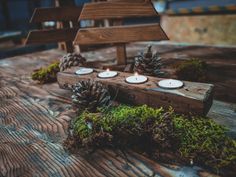 three candles are placed on a wooden table with moss and pineconis around them