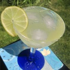 a blue glass filled with lemonade sitting on top of a table next to a green grass covered field