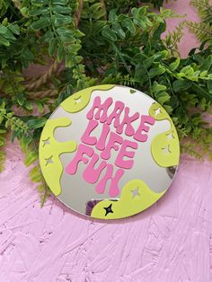 a circular mirror with the words make life fun painted on it next to some green leaves