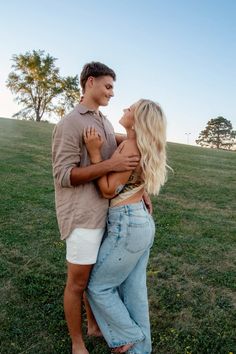 a man and woman standing in the grass with their arms around each other as they hug