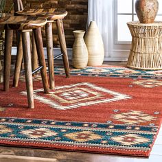 a red rug with blue and white designs on it in front of a window next to wooden stools