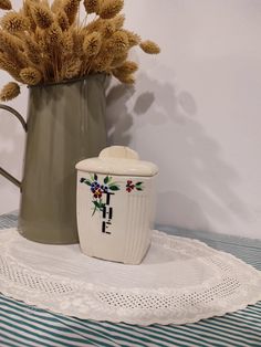 there is a vase with flowers in it next to a coffee pot on a doily