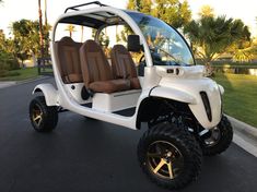 a white golf cart with brown leather seats parked in a parking lot next to palm trees