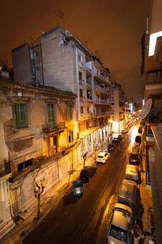 a city street at night with cars parked on both sides and buildings in the background