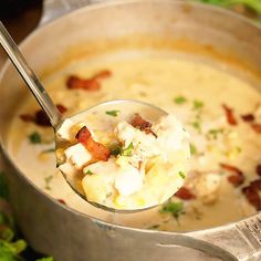 a spoon full of potato soup with bacon and cheese on top, in a pot