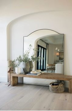 a mirror sitting on top of a wooden table next to a vase filled with plants