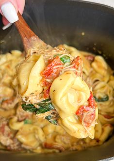 someone is stirring some pasta with spinach and tomato sauce in a pan on the stove