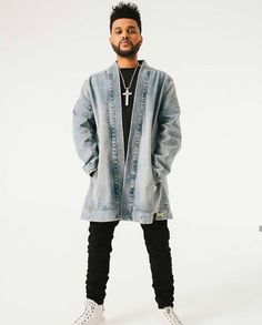 a man standing in front of a white background wearing a denim jacket and black pants