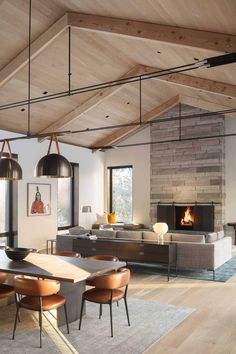 an open concept living room and dining area with wood flooring, exposed brick fireplace, modern furniture and large windows