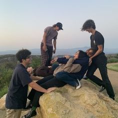 four people standing around a woman laying on top of a rock