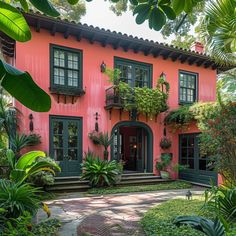 a pink house with green shutters and potted plants on the front porch, surrounded by greenery