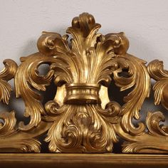 an ornate gold frame on top of a wooden shelf with white walls in the background