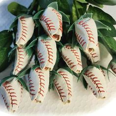 dozen baseballs are arranged on a white plate next to some green leaves and flowers