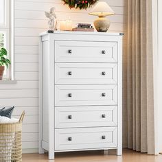 a white chest of drawers sitting next to a christmas wreath on top of a window sill