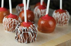 caramel apples with white chocolate drizzle and candy on top are sitting on a wooden tray