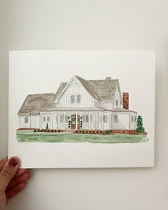 a person holding up a drawing of a white house in front of a white wall