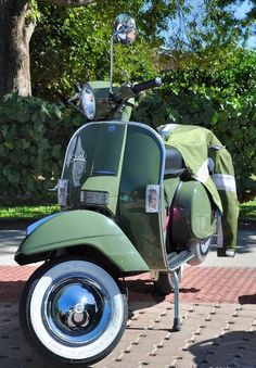 a green scooter parked on the side of a brick road next to a tree