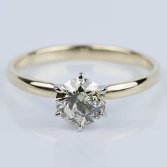 a yellow gold engagement ring with a round cut diamond in the center, on a white background